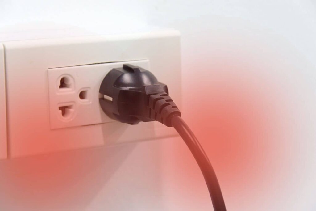A close-up view shows a black electrical plug inserted into a white wall outlet with a soft red glow overlay around the lower edges.